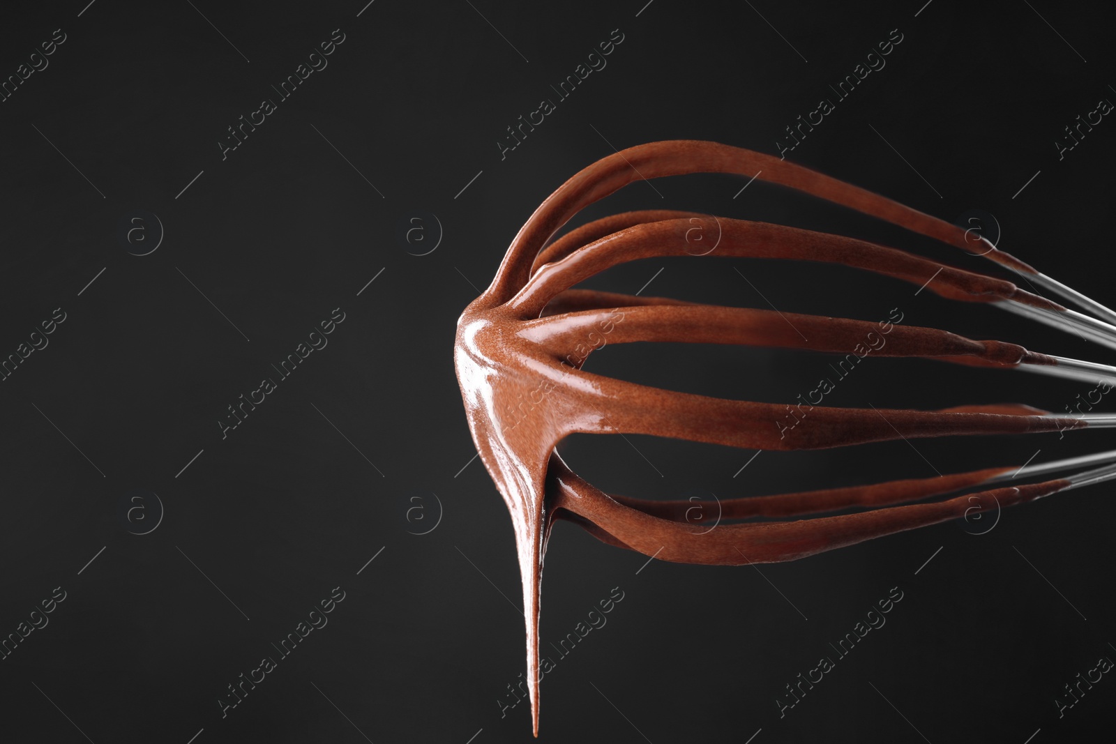 Photo of Chocolate cream flowing from whisk on black background, closeup. Space for text