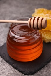 Photo of Sweet golden honey in jar and dipper on grey table, closeup