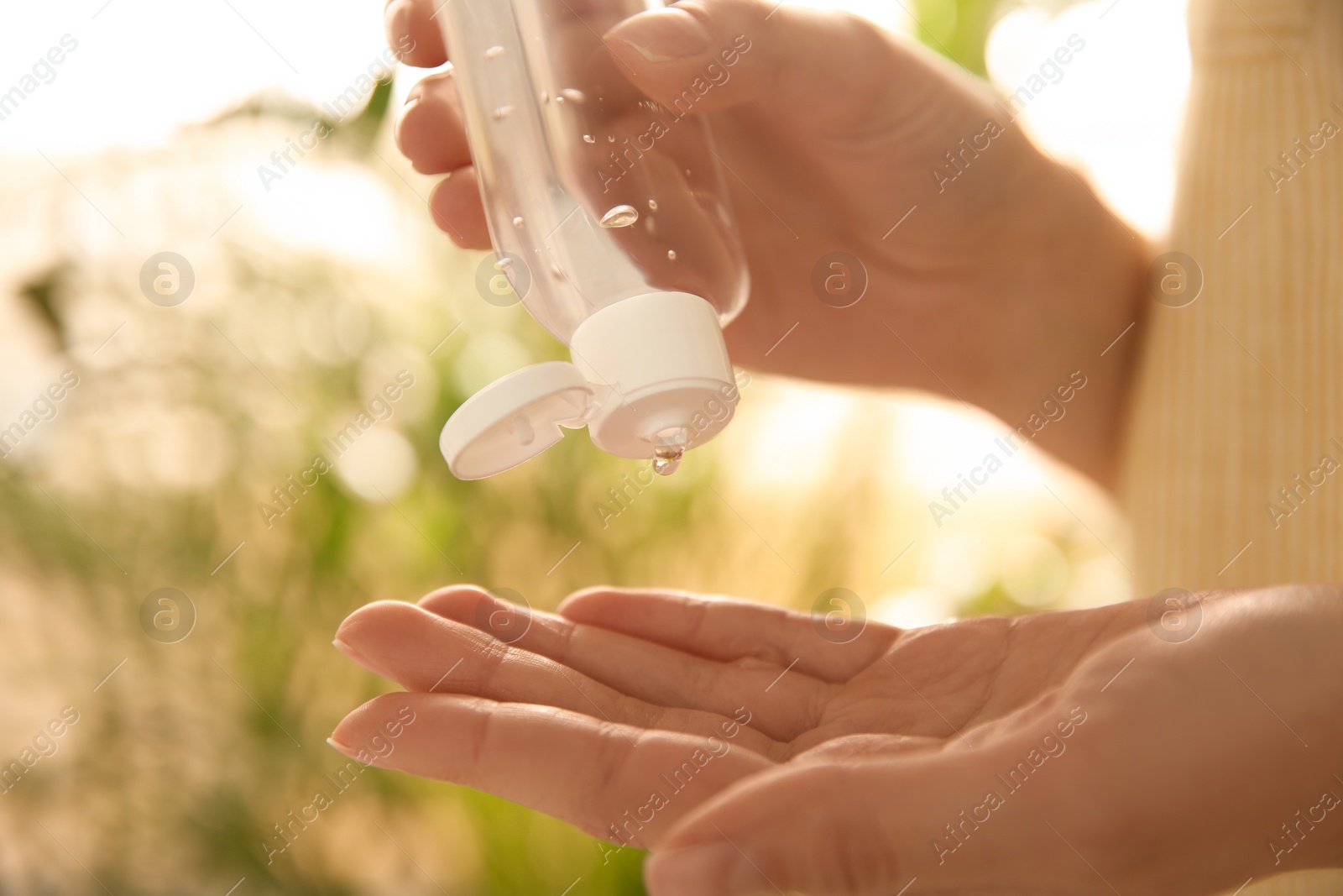 Photo of Young woman applying antiseptic gel outdoors, closeup