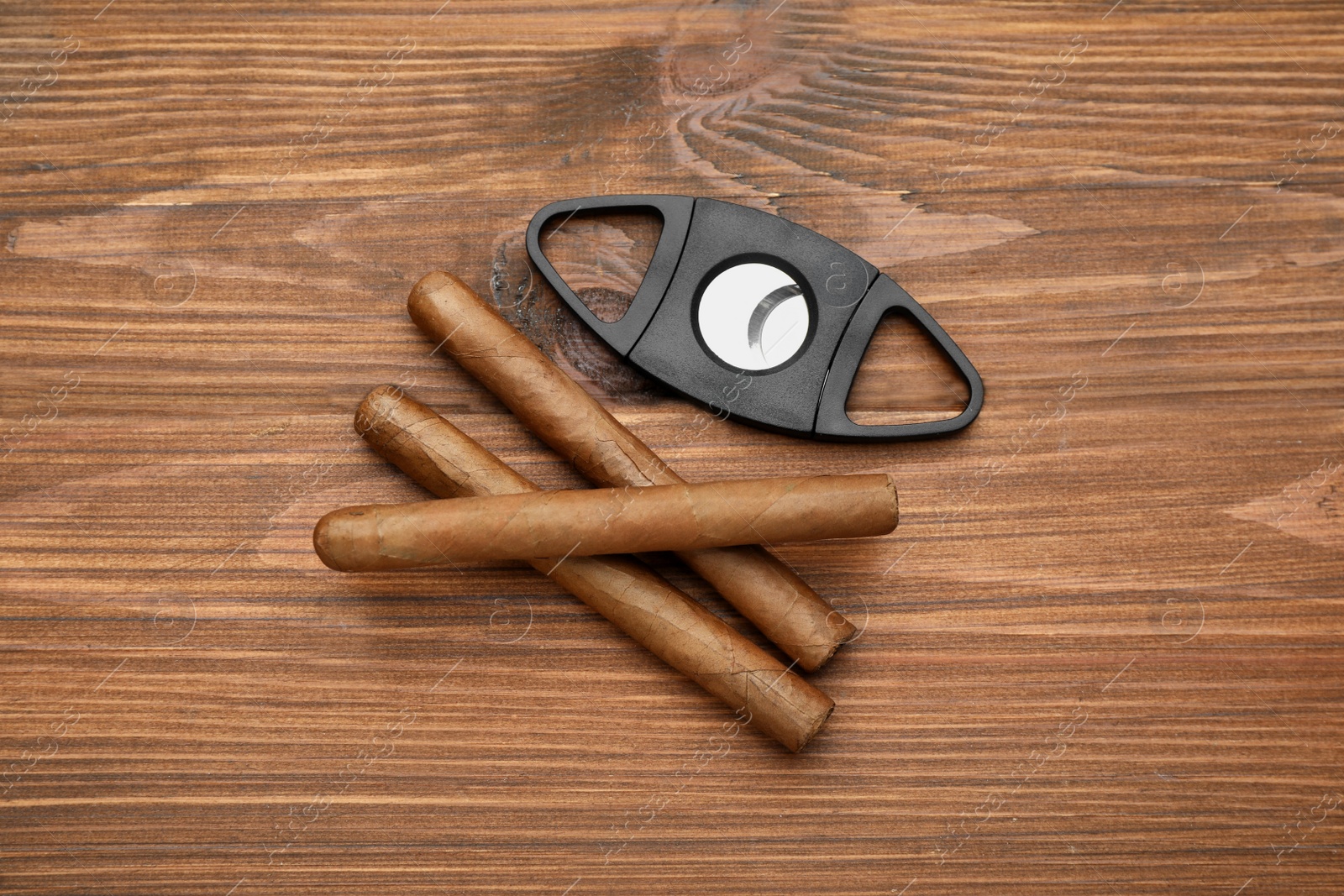 Photo of Cigars and guillotine cutter on wooden table, flat lay