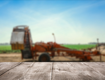 Image of Empty wooden surface and blurred view of modern agricultural equipment in field. Space for text