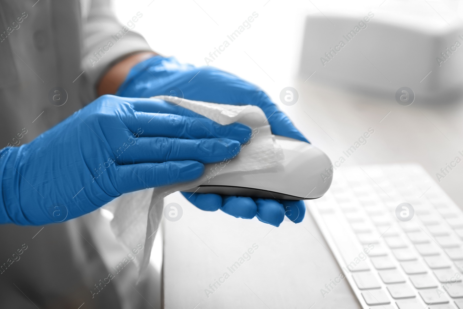 Photo of Woman in latex gloves cleaning computer mouse with wet wipe at table, closeup