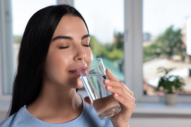 Photo of Young woman drinking water indoors. Refreshing drink