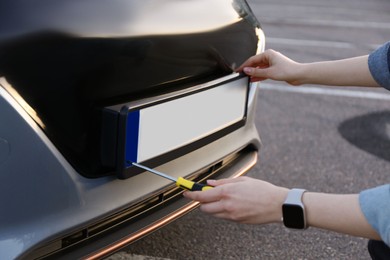 Woman with screwdriver installing vehicle registration plate to car outdoors, closeup