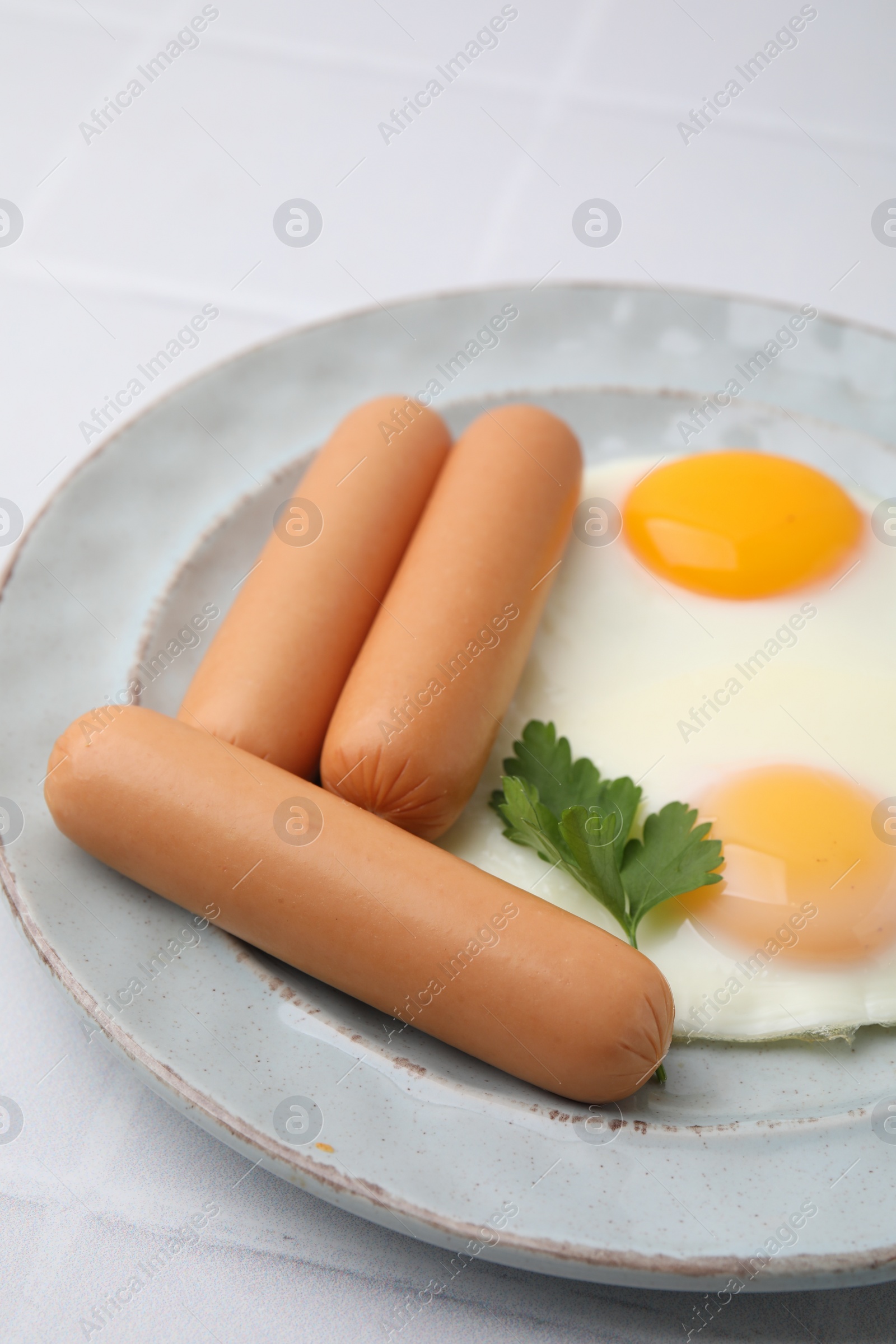 Photo of Delicious boiled sausages, fried eggs and parsley on white table, closeup