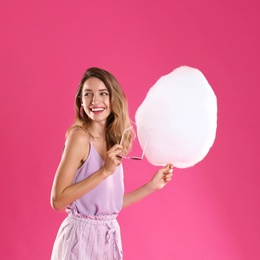 Happy young woman with cotton candy on pink background