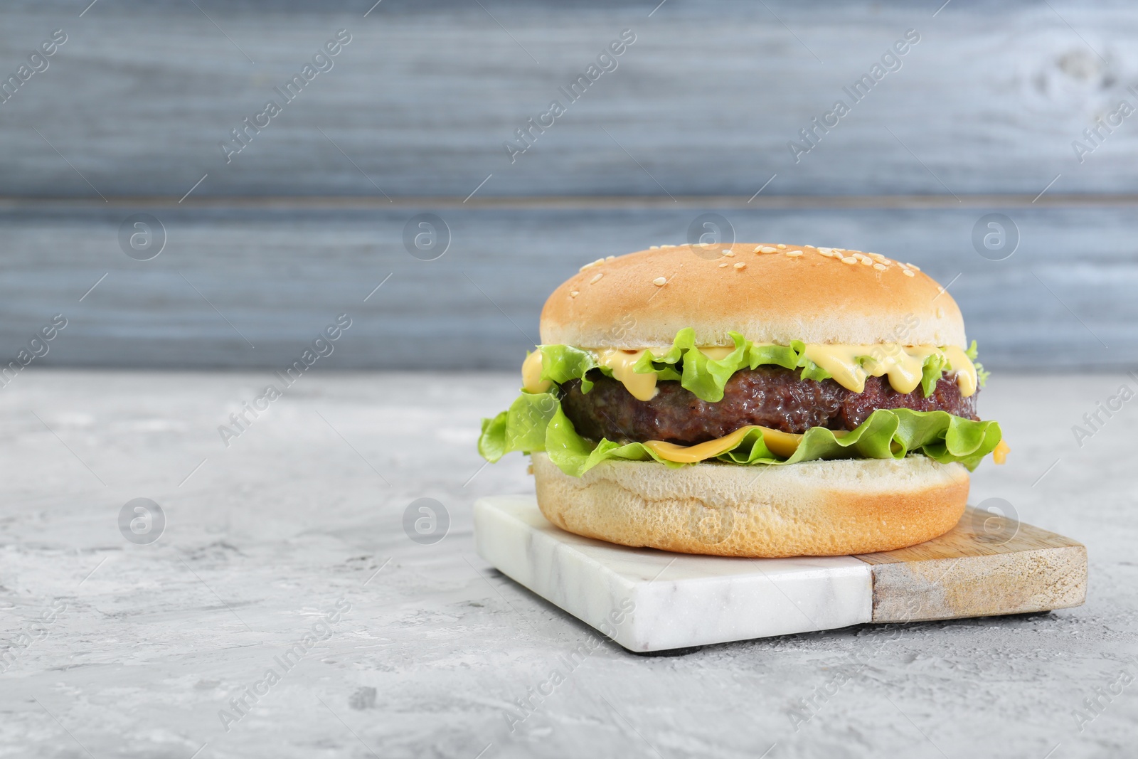 Photo of Delicious cheeseburger on grey textured table, closeup. Space for text