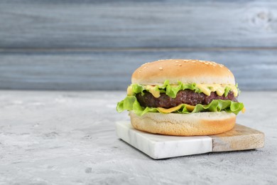 Photo of Delicious cheeseburger on grey textured table, closeup. Space for text