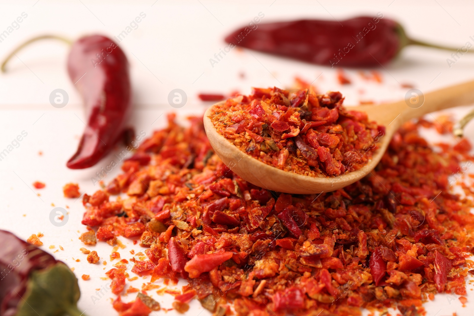 Photo of Chili pepper flakes and pods on white wooden table, closeup