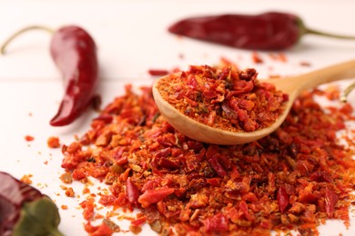 Chili pepper flakes and pods on white wooden table, closeup