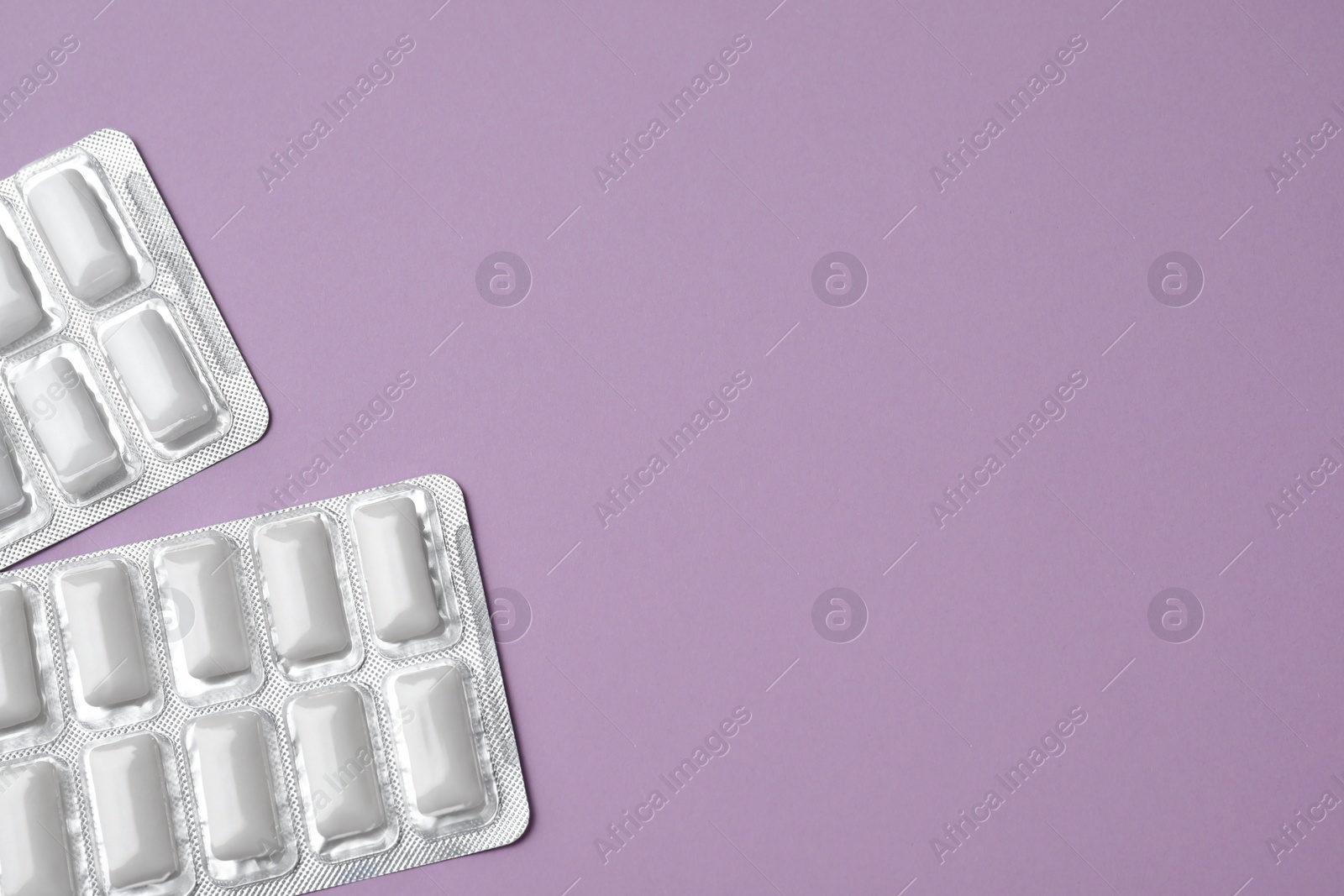 Photo of Blisters of tasty chewing gums on violet background, flat lay. Space for text