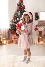 Photo of Cute little child in Santa hat with Christmas gift box at home