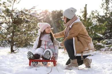 Photo of Young woman and her daughter with sledge outdoors on winter day. Christmas vacation