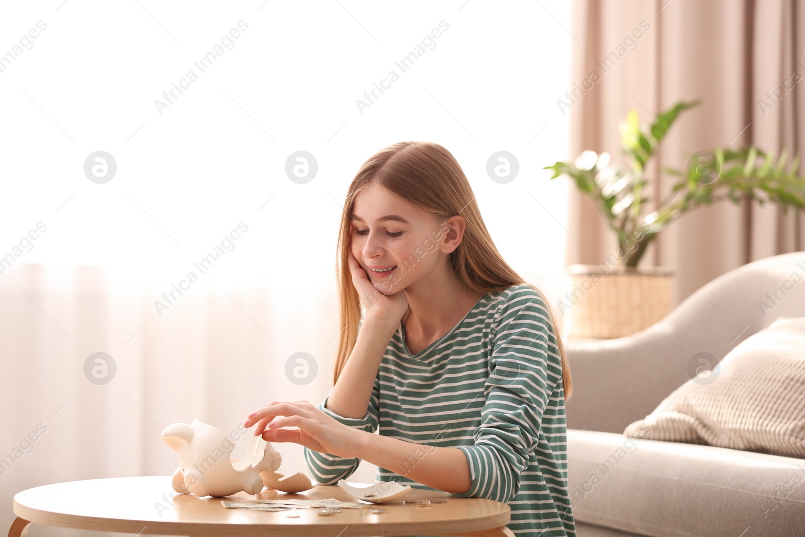 Photo of Teen girl with broken piggy bank and money at home