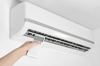Photo of Woman operating air conditioner with remote control indoors, closeup