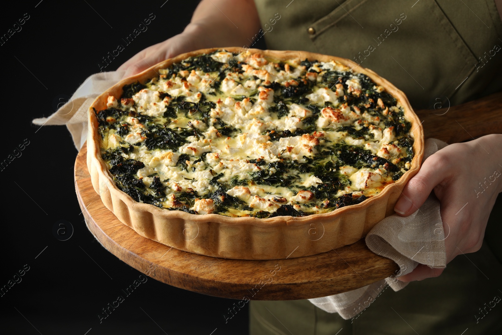 Photo of Woman holding delicious homemade spinach quiche on dark background, closeup