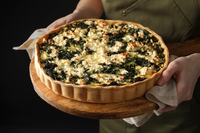 Woman holding delicious homemade spinach quiche on dark background, closeup