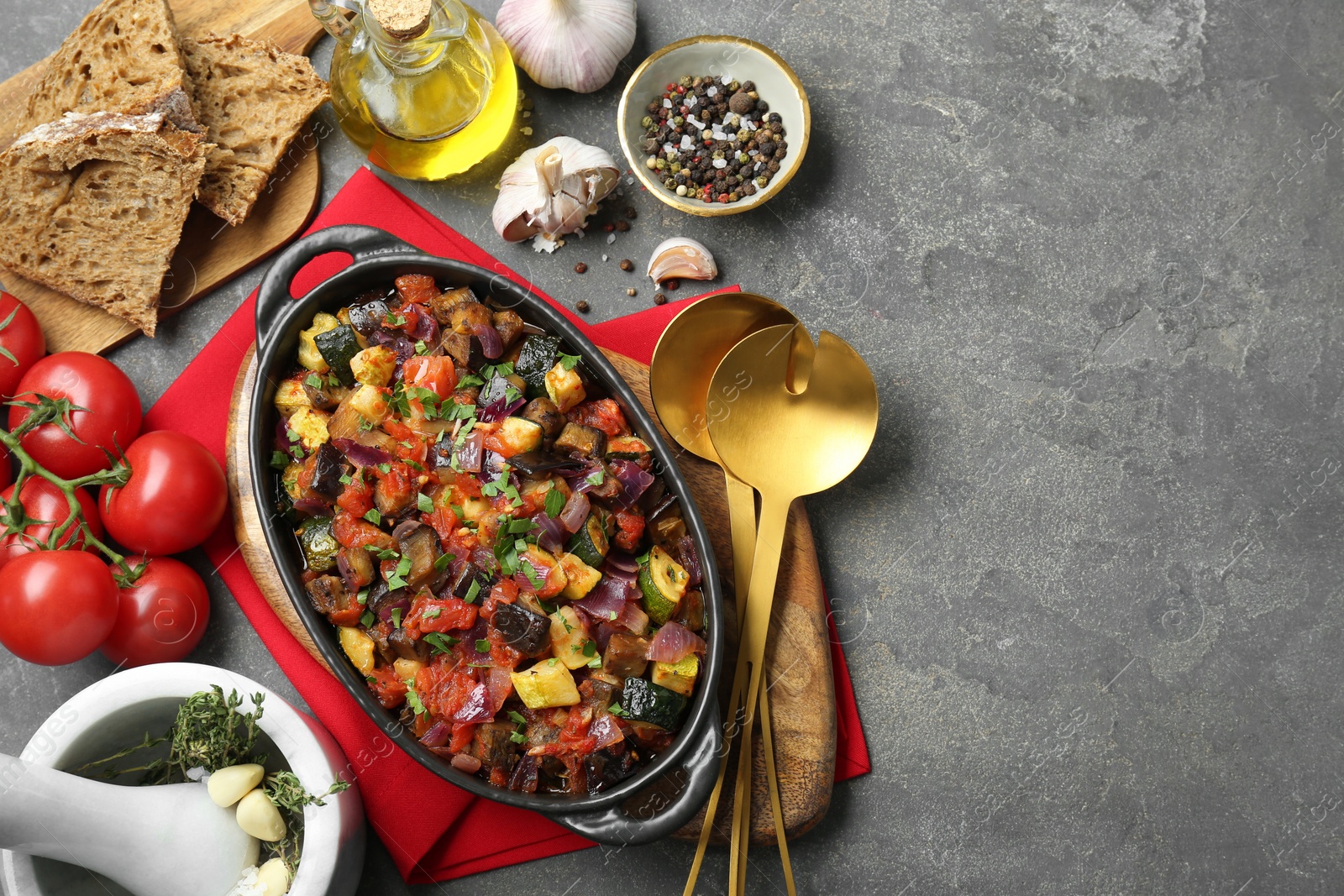 Photo of Dish with tasty ratatouille, ingredients and bread on grey textured table, flat lay. Space for text