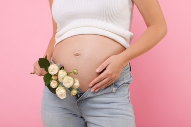 Pregnant woman with roses on pink background, closeup