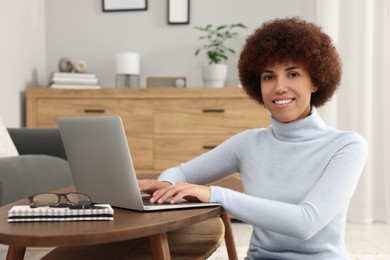 Photo of Beautiful young woman using laptop at wooden coffee table in room