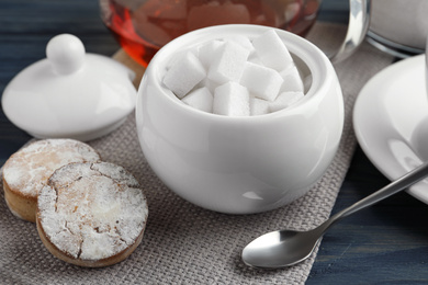 Photo of Refined sugar cubes in ceramic bowl on blue wooden table