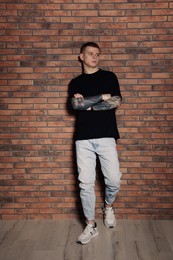 Young man with tattoos near brick wall