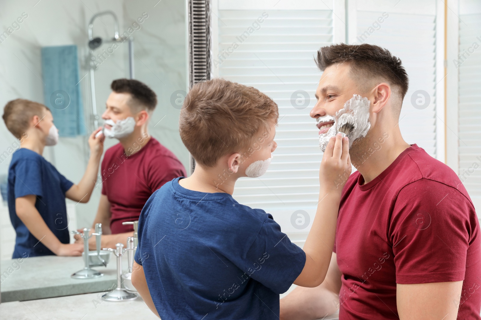 Photo of Son applying shaving foam on dad's face at mirror in bathroom