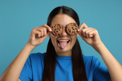 Young woman with chocolate chip cookies on light blue background