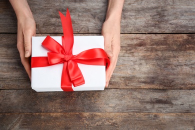 Photo of Young woman holding beautiful gift box on wooden background, top view