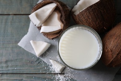 Glass of delicious coconut milk, flakes and nuts on wooden table, flat lay. Space for text