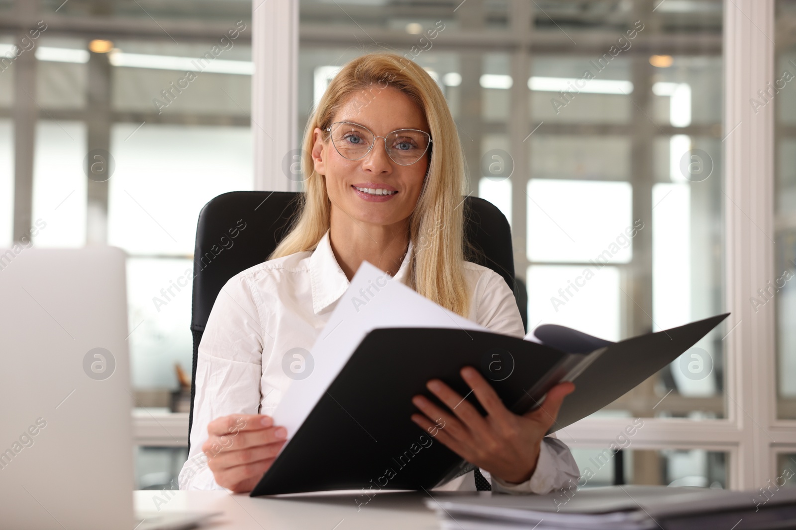 Photo of Smiling woman working at table in office. Lawyer, businesswoman, accountant or manager