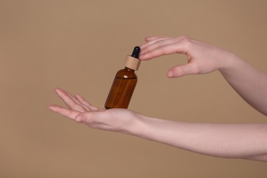 Photo of Woman holding bottle of essential oil on brown background, closeup