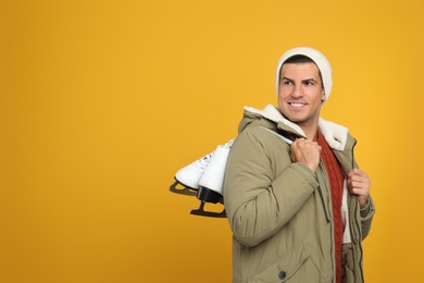 Photo of Happy man with ice skates on yellow background. Space for text