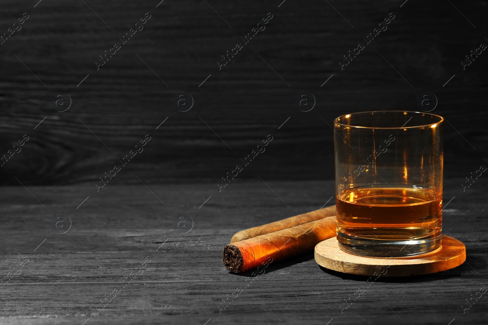 Photo of Glass of whiskey and cigars on black wooden table. Space for text