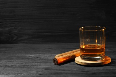 Photo of Glass of whiskey and cigars on black wooden table. Space for text