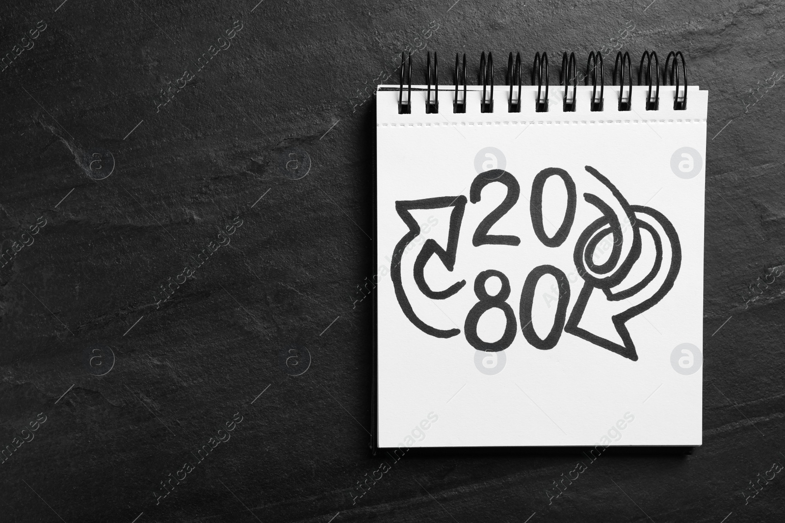 Photo of Top view of notebook with numbers 20, 80 and arrows on black slate background, space for text. Pareto principle concept