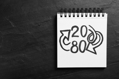 Photo of Top view of notebook with numbers 20, 80 and arrows on black slate background, space for text. Pareto principle concept