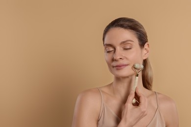 Photo of Woman massaging her face with jade roller on beige background. Space for text
