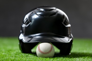 Photo of Batting helmet and baseball ball on green grass against dark background, closeup