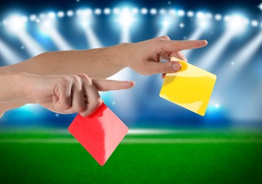 Referee holding red and yellow cards at stadium, closeup