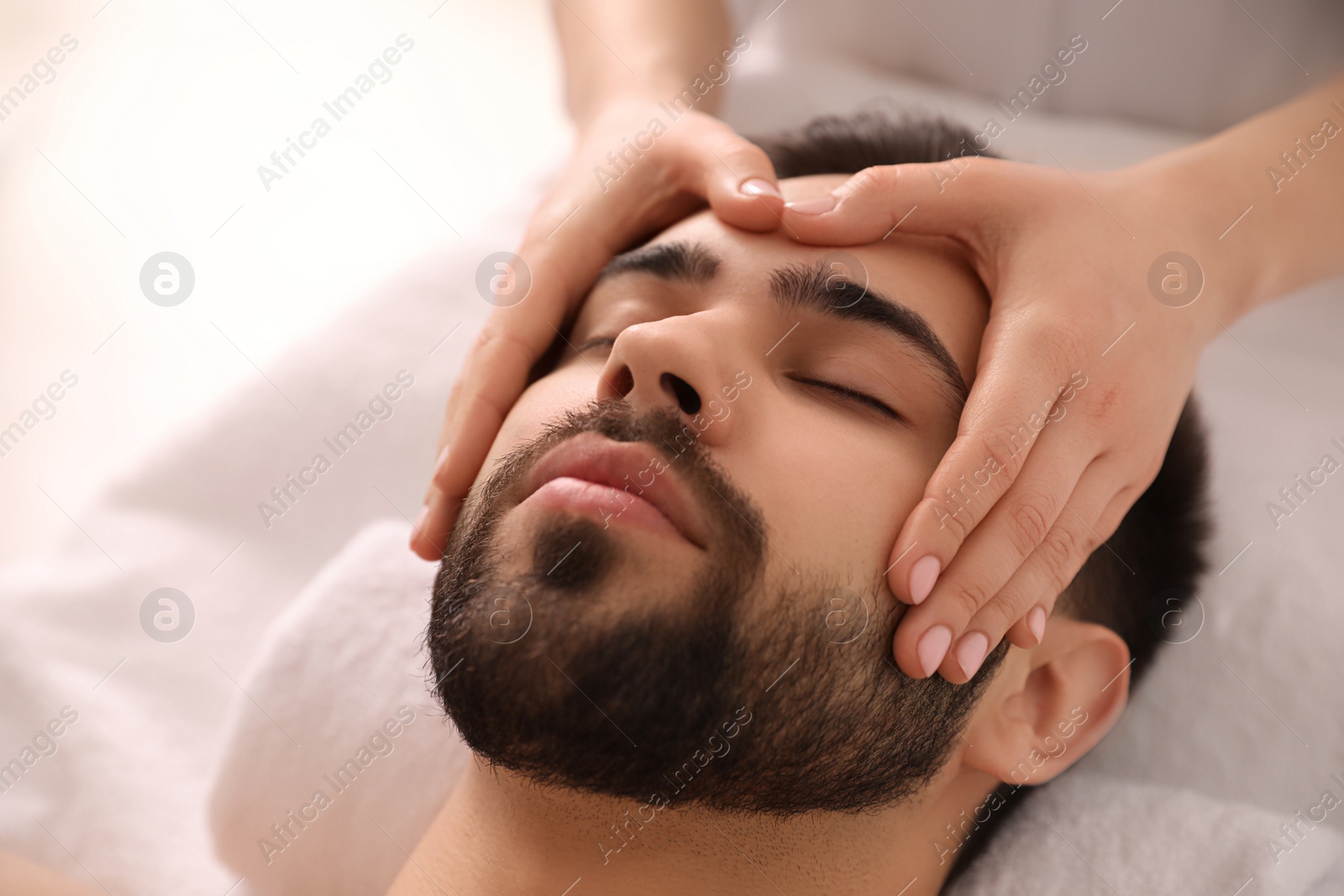 Photo of Young man receiving facial massage in beauty salon, closeup