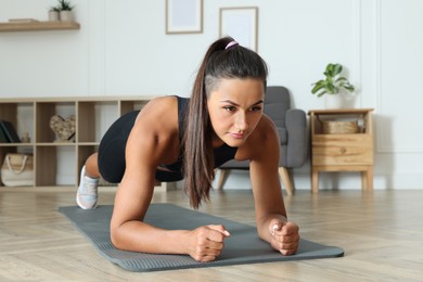 Photo of Young woman doing plank exercise on floor indoors