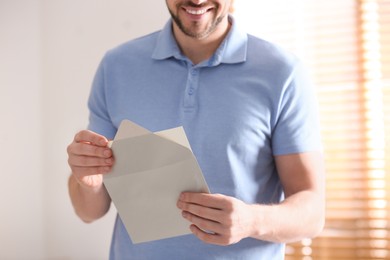 Man holding envelope with blank greeting card indoors. closeup