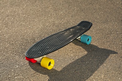 Photo of Black skateboard with colorful wheels on asphalt outdoors