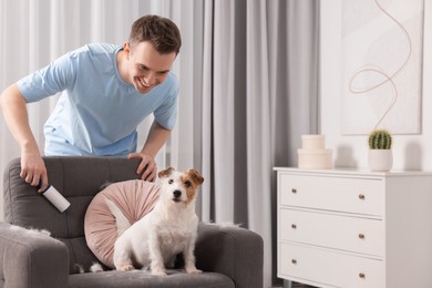 Photo of Smiling man removing pet's hair from armchair at home. Space for text