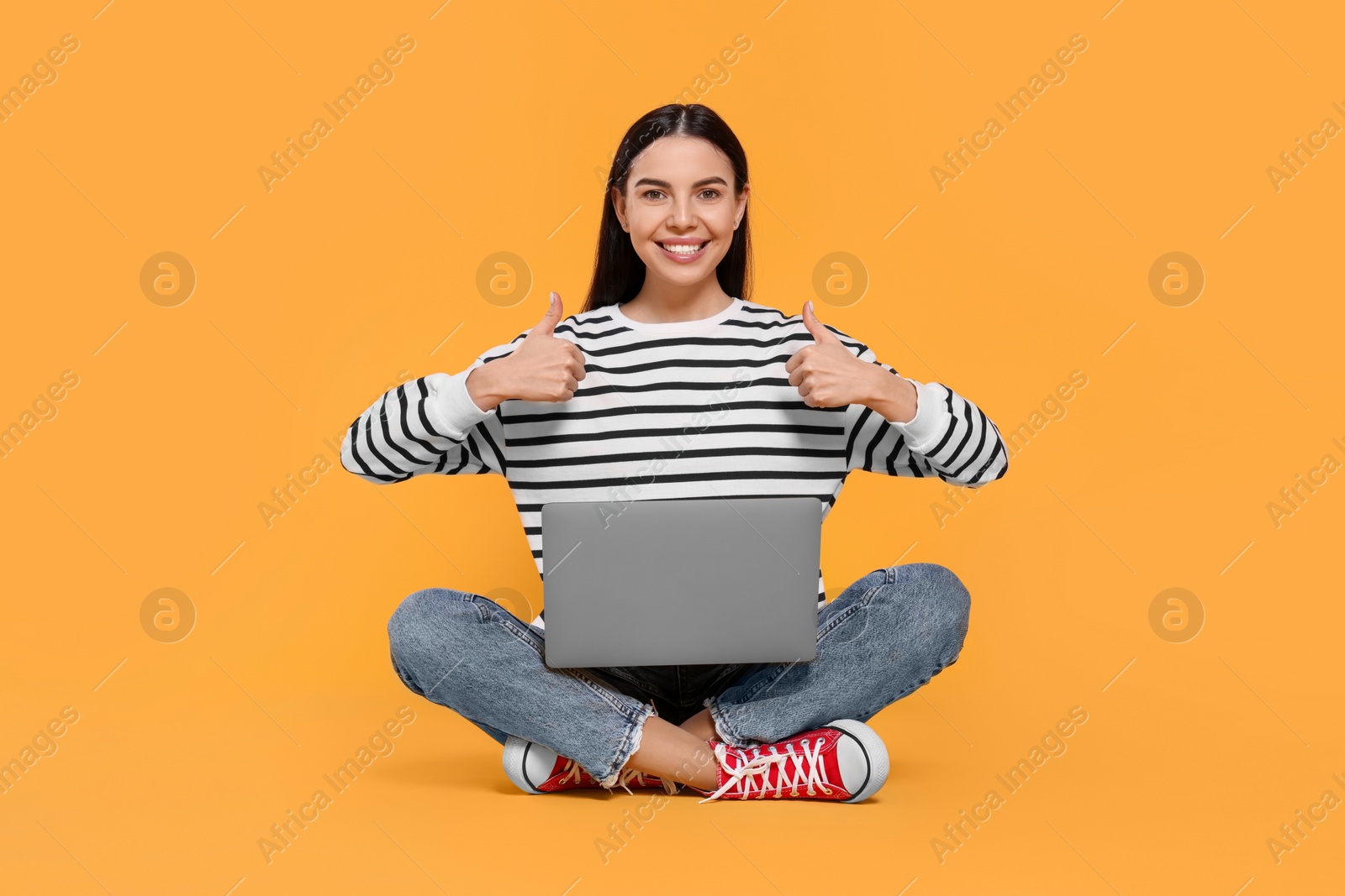 Photo of Happy woman with laptop showing thumbs up on orange background