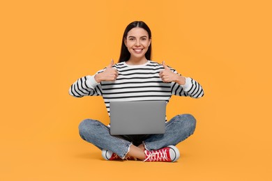 Photo of Happy woman with laptop showing thumbs up on orange background