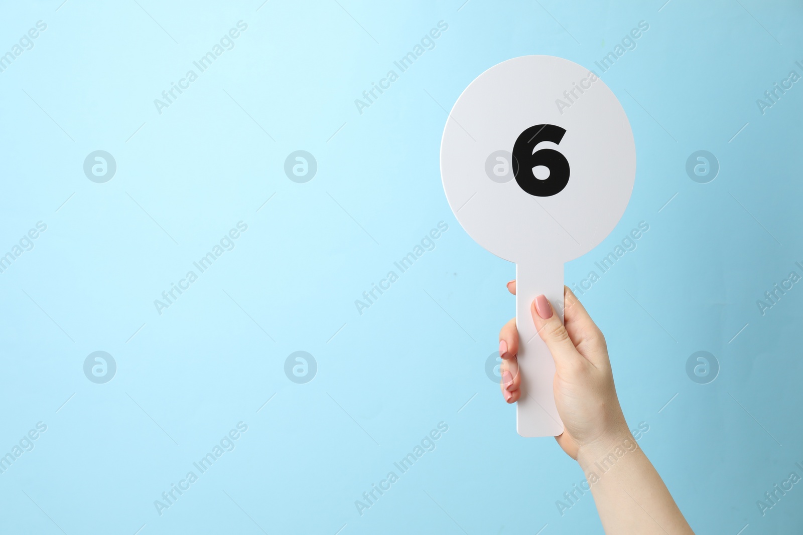 Photo of Woman holding auction paddle with number 6 on light blue background, closeup. Space for text