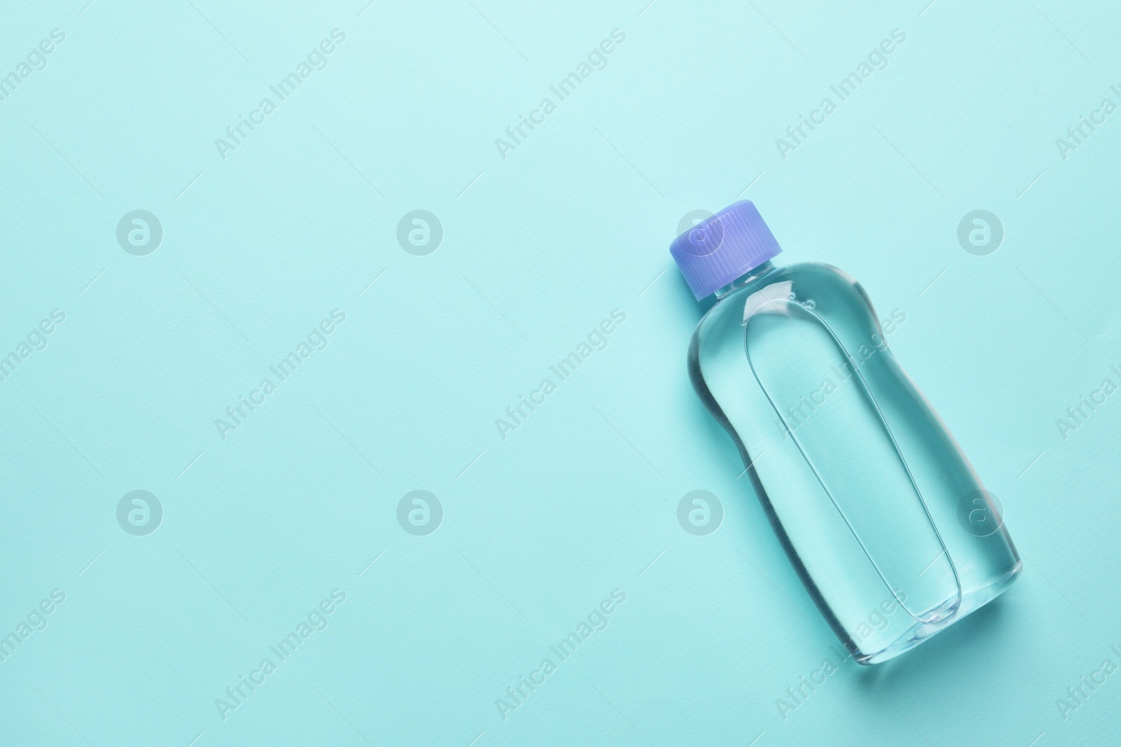 Photo of Bottle of baby oil on turquoise background, top view. Space for text