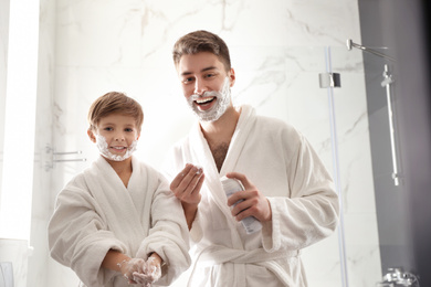Photo of Dad and son with shaving foam on their faces having fun in bathroom